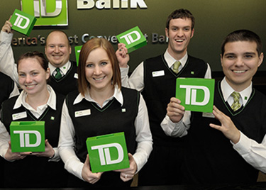 A group of happy TD Bank employees holding TD bank logos